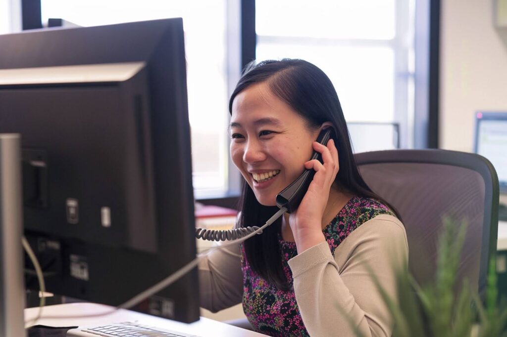 Female Asian outsourced medical secretary working on her computer and talking on the phone