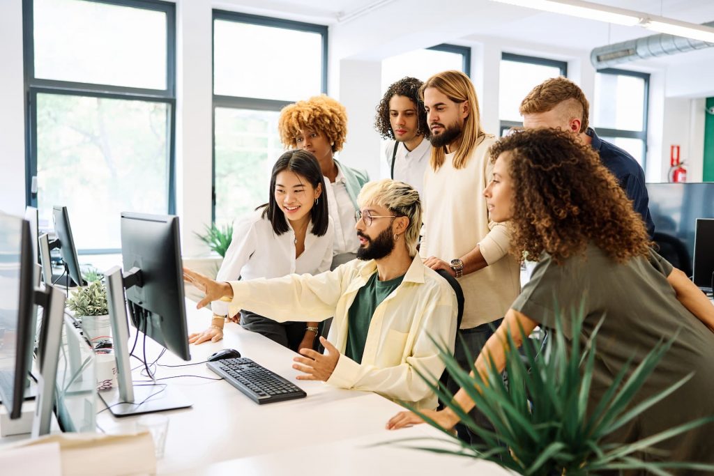 A multicultural team of IT specialists collaborating closely around a desktop computer