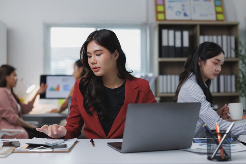 身著紅外套的女士在筆記型電腦前工作 — 業務流程外包與離岸人力資源服務 |Sourcefit
