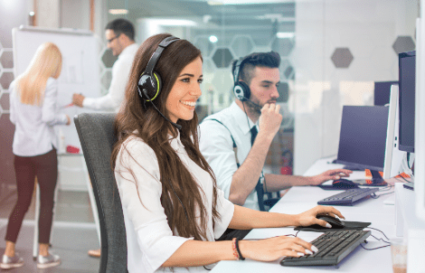Young positive woman customer support phone operator in microphone headset working on computer in the office